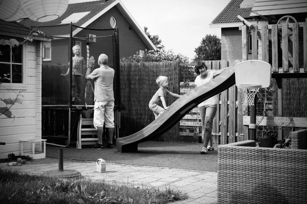 kleinzoontjes spelen in de tuin met Opa en Oma, op de glijbaan en de trampoline, in het zomerseizoen.