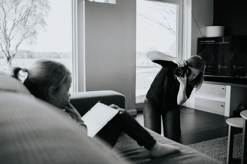 Behind the scenesfoto van ellenklikt die een documentaire gezinsshoot doet bij mensen thuis. Ellen fotografeert een kleuter die op de bank een filmpje kijkt op de tablet.