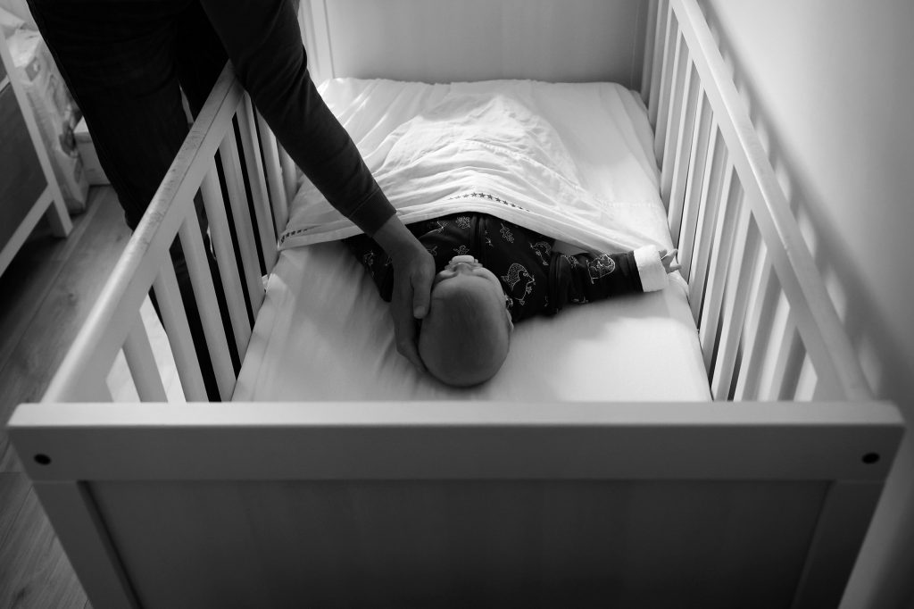 zwart-witfoto van een documentaire gezinsshoot van ellenklikt. Een babymeisje ligt in haar ledikantje, vader aait haar over het bolletje om welterusten te zeggen.